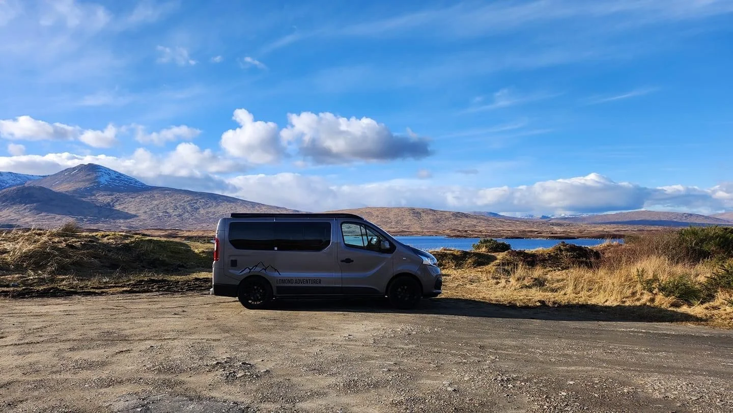 Lomond Campers Ultimate Guide On Campervans showing the lifestyle with a picture of a campervan on a beautiful nature backdrop of blue skies, a lake and distant mountains.